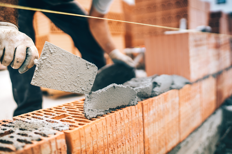 builder laying cement on bricks to build a house